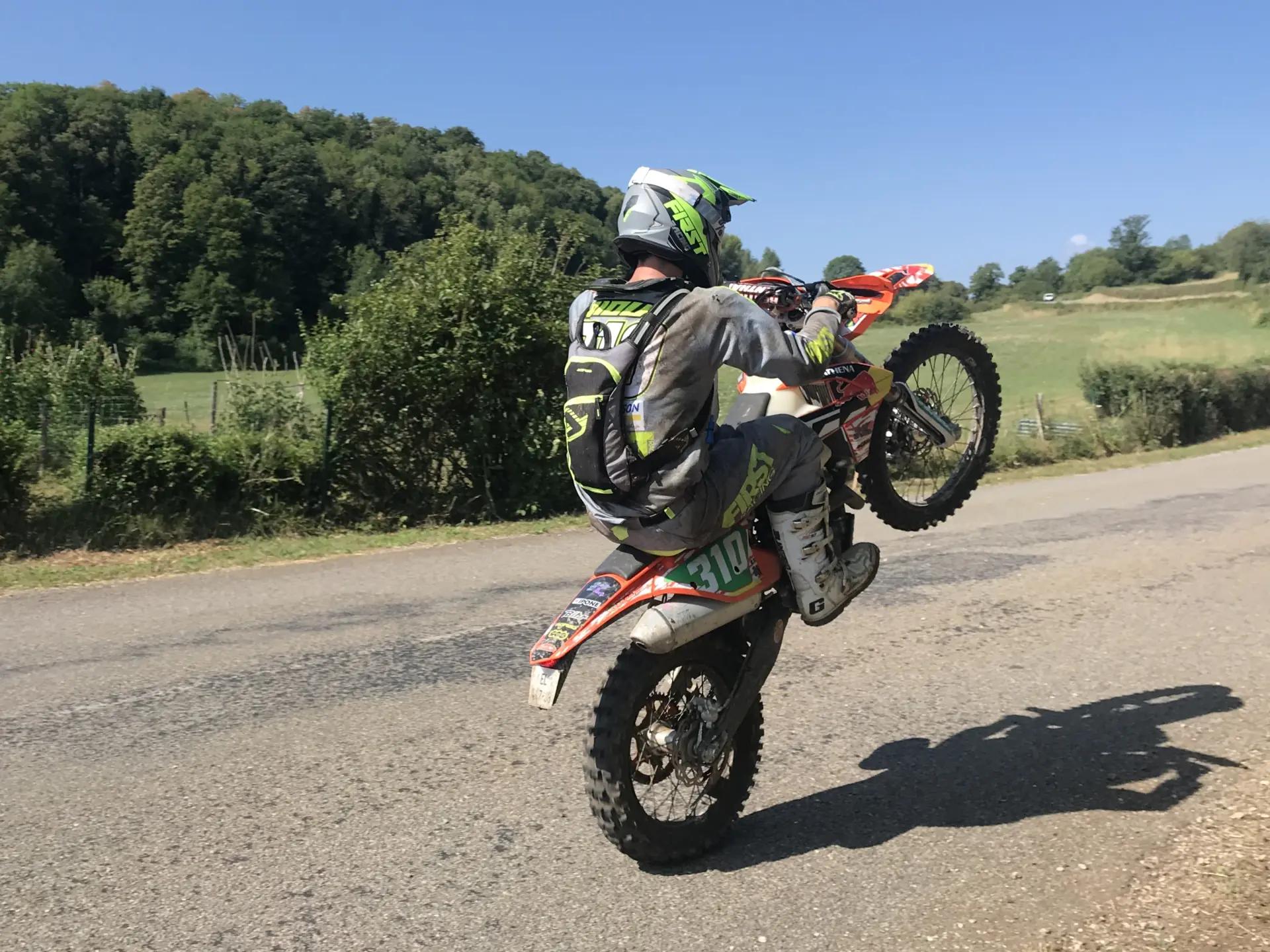 Un pilote d'enduro sur une route de campagne, plaque numéro sur le flanc de la moto.